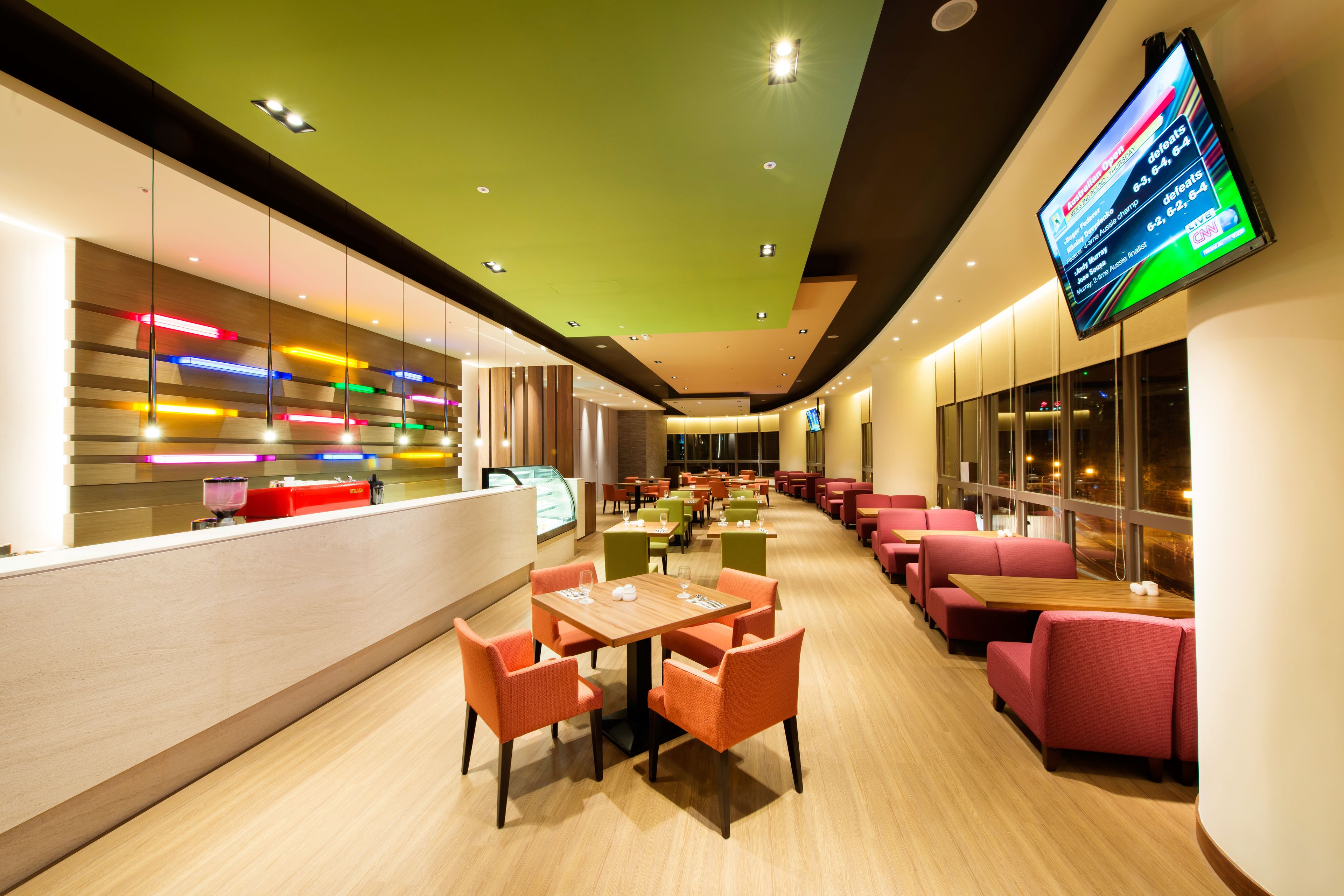 Um restaurante moderno com um balcão extenso, várias mesas e cabines. Há uma tela exibindo o cardápio.