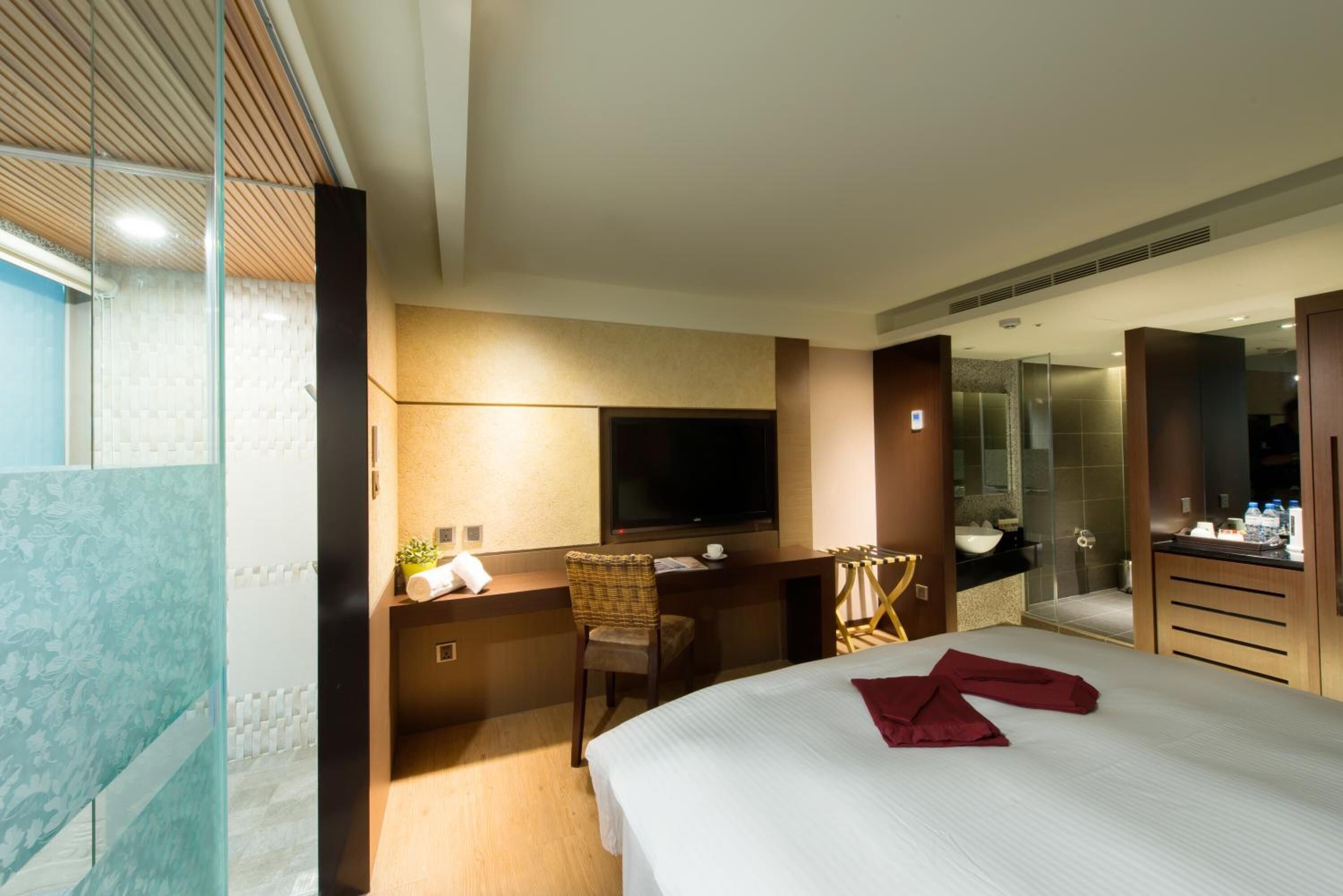 A hotel room with a bed, a desk with a chair, a television, a shower area, and a bathroom.
