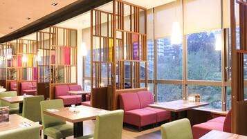 A modern restaurant with booths and tables, large windows, and a view of the city.