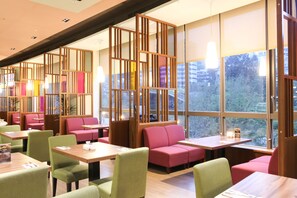 A modern restaurant with booths and tables, large windows, and a view of the city.