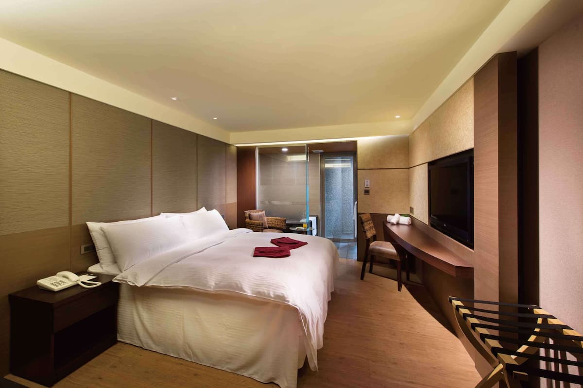 A hotel room with a large bed, a desk with a chair, a television, and a phone on a nightstand.