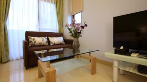 A modern living room with a glass coffee table, a brown sofa with patterned cushions, a vase with flowers, and a flat-screen TV on a stand. - Hualien Little Squirrel B&b (Hualien City)