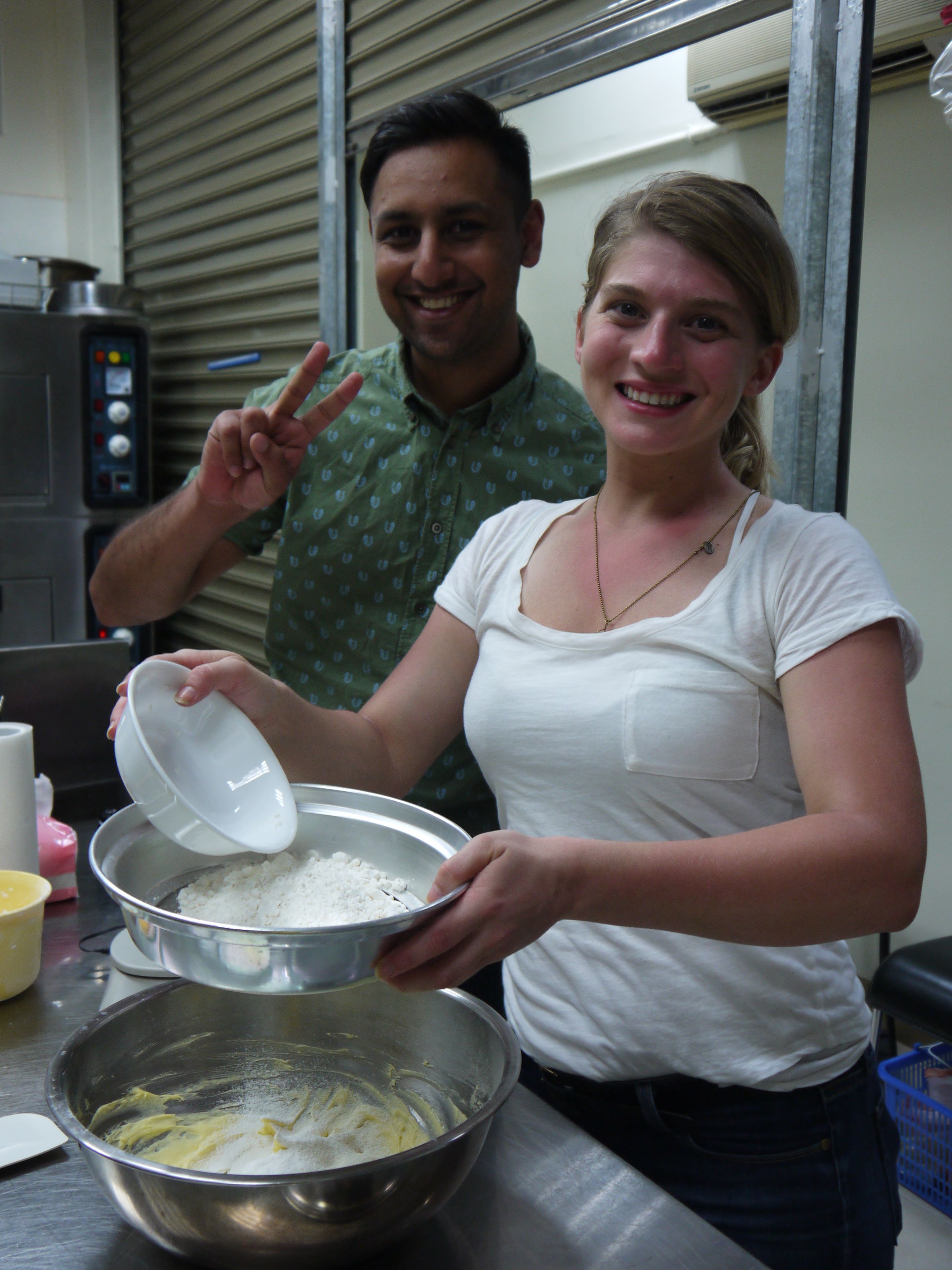 A person holding a bowl with a white substance, possibly flour, in a kitchen setting with stainless steel appliances.