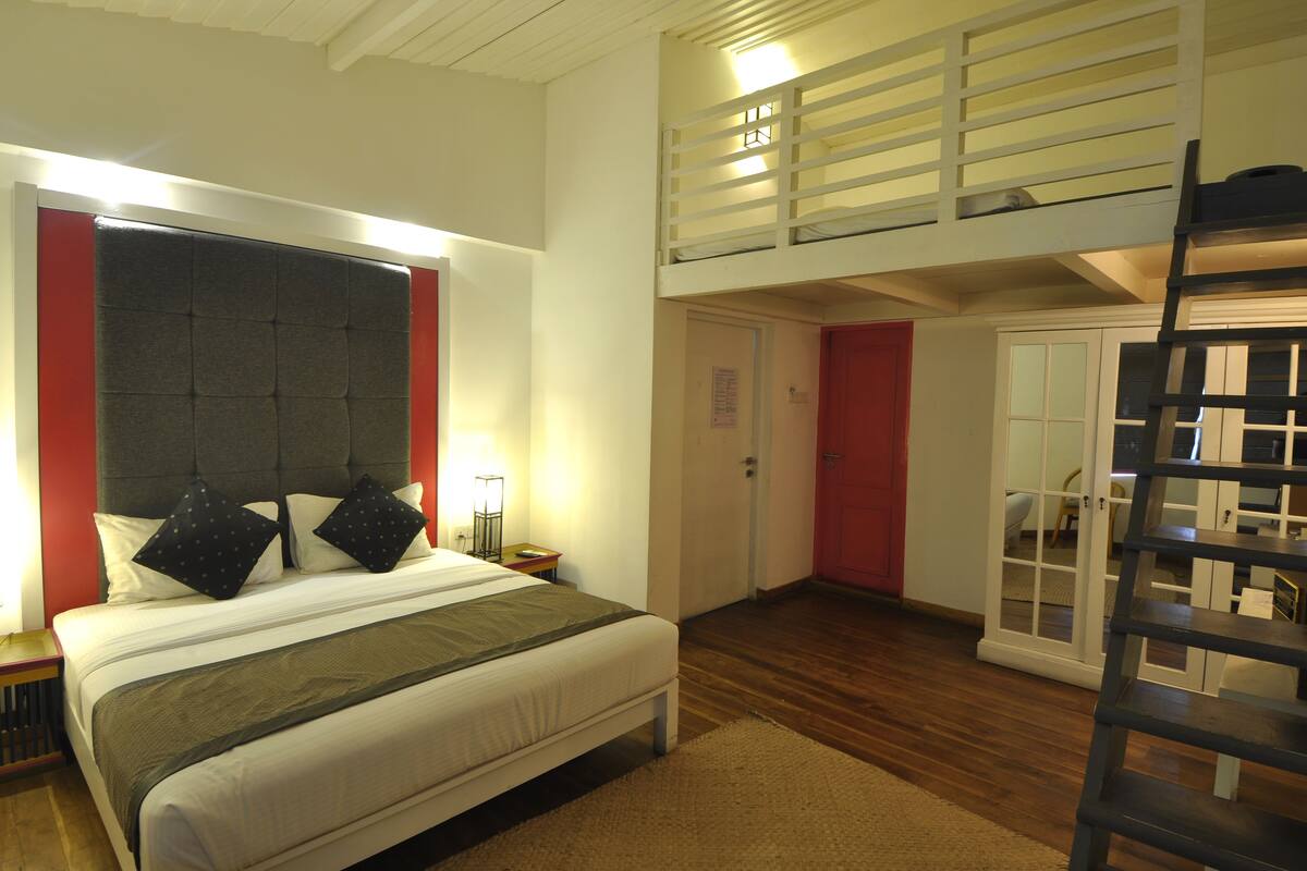 A bedroom with a large bed, a loft area, and a wooden floor.