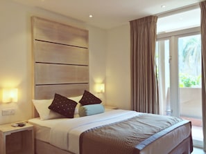 Ein Hotelzimmer mit einem großen Bett, zwei Nachttischen, einem Wandpaneel als Kopfteil und Blick ins Freie durch eine Schiebetür.