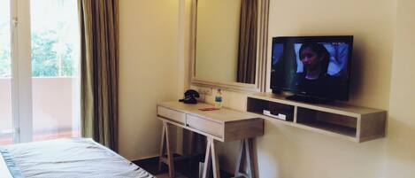 A hotel room with a bed, a desk with a telephone, a television, and an air conditioning unit.