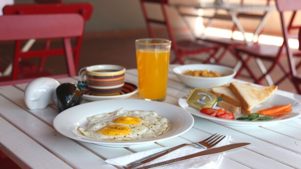 A breakfast table with plates of eggs, toast, and vegetables, a glass of orange juice, and a mug. - Ivy Lane Colombo (Colombo)