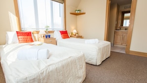 A hotel room with two beds, a window, a small table with a lamp, and a wooden shelf above the door. - Kamakura (Kutchan)