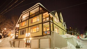 A multi-story building with a balcony on the second floor, a garage, and a snow-covered ground. - Kamakura (Kutchan)