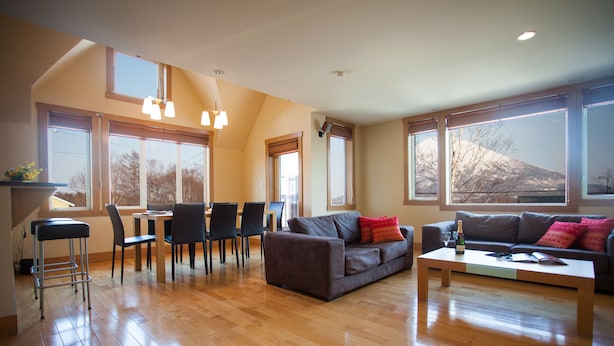 A spacious living room with a wooden floor, a sofa, a coffee table, and a dining area with chairs and a table. - Kamakura (Kutchan)