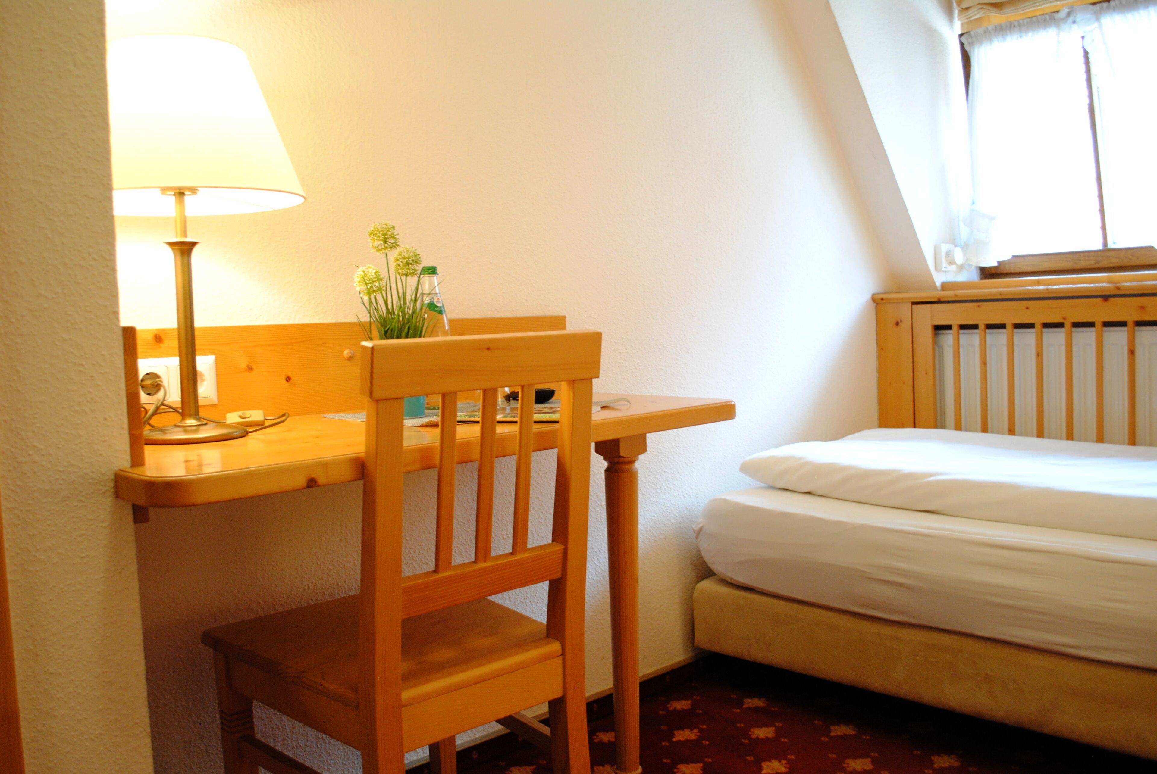 Una habitación pequeña y acogedora con un escritorio de madera, una silla, una lámpara y una cama.