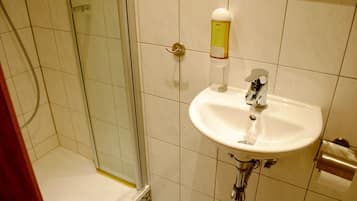 Een badkamer met een douche met glazen wand, een witte wastafel en een zeepdispenser aan de muur.