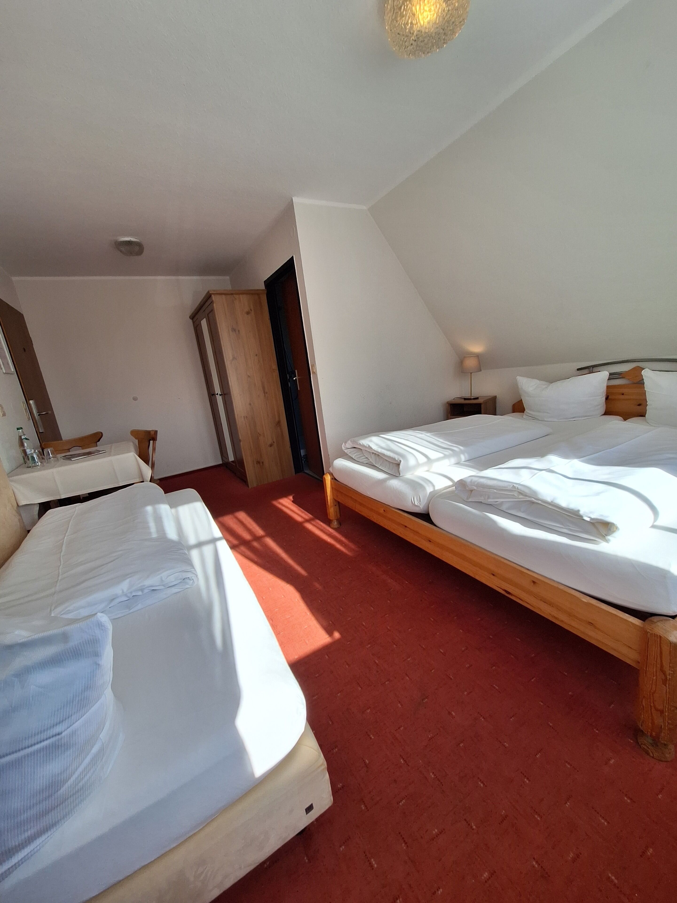 Una habitación de hotel con dos camas, un armario de madera, un escritorio con una silla y una mesita de noche con lámpara.