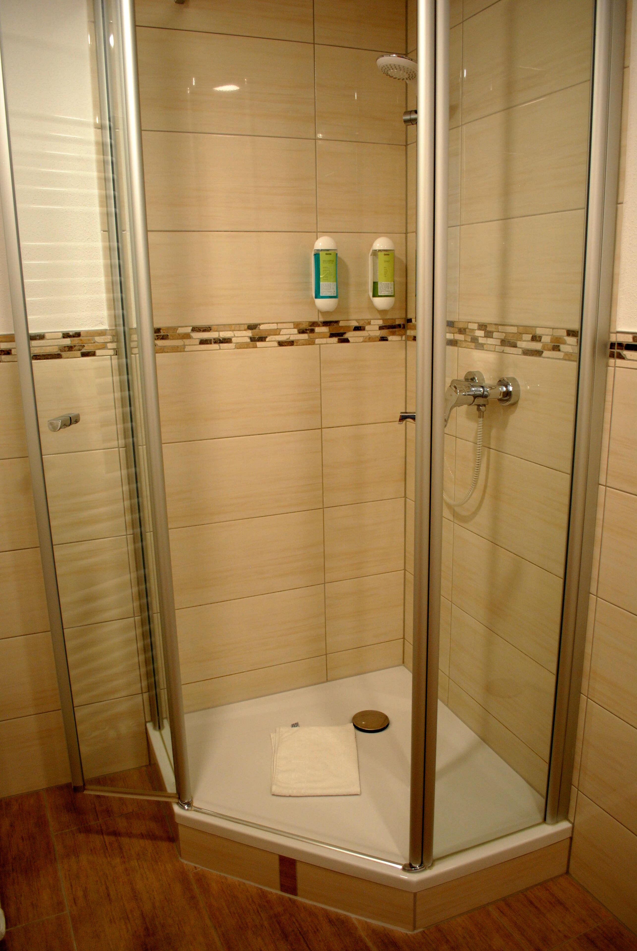 A glass-enclosed shower stall with a tiled floor and a small shelf holding toiletries.
