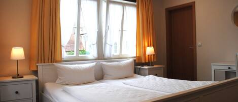A neatly made bed with white linens, two bedside tables with lamps, and a window with curtains.