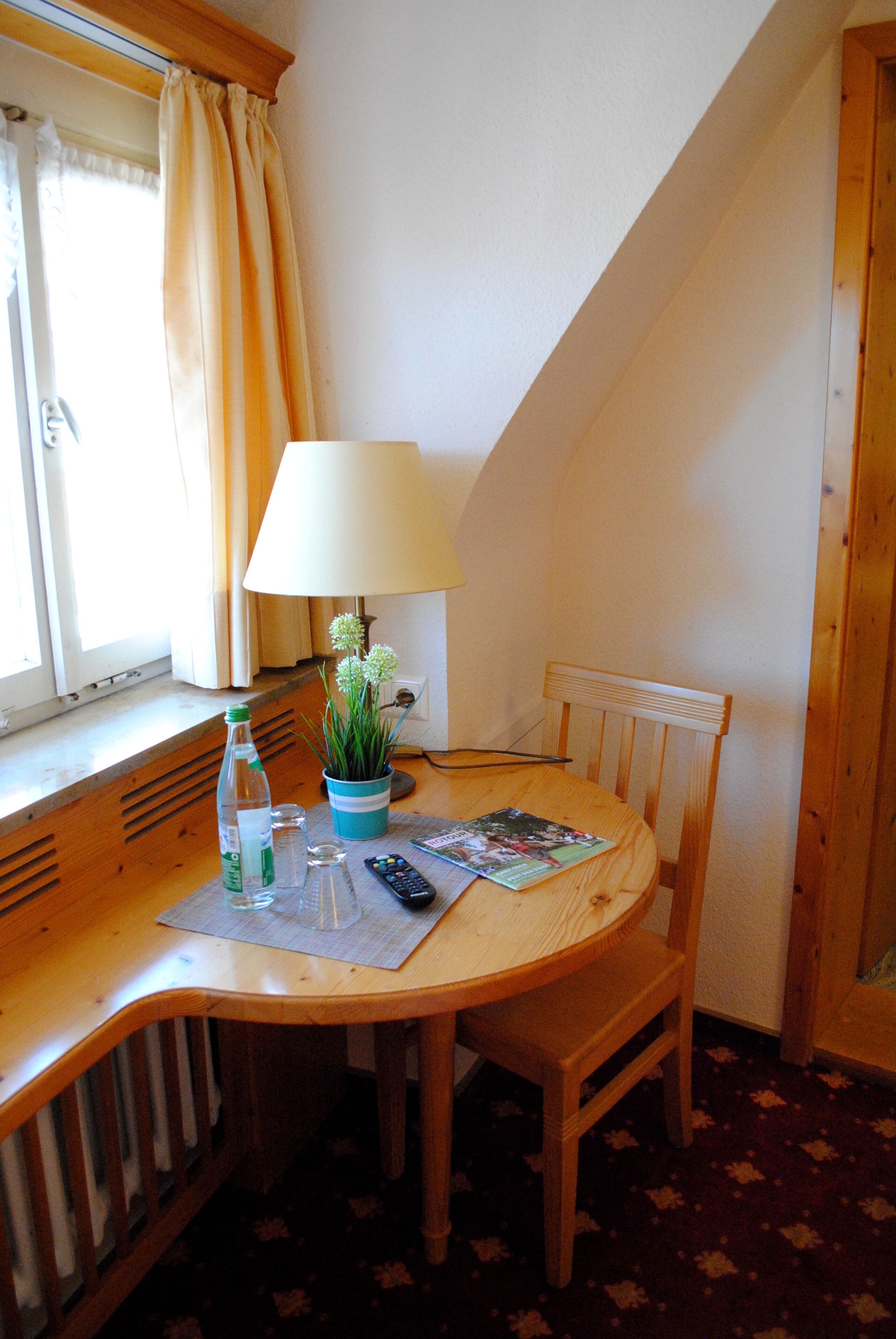 A small wooden table with a lamp, a potted plant, a remote control, and a magazine.