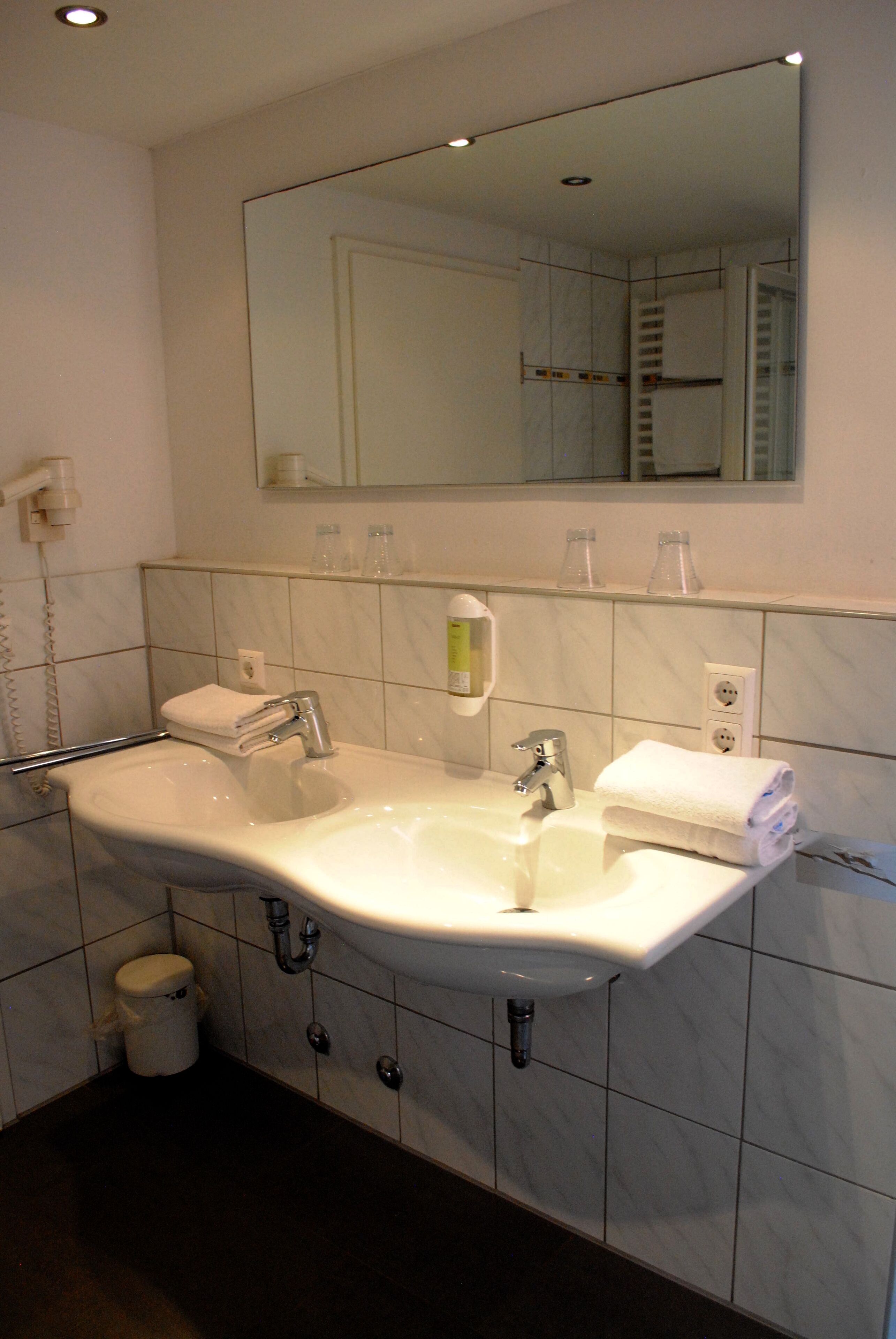 Un baño con un lavamanos grande, dos toalleros, un espejo y un cubo de basura.