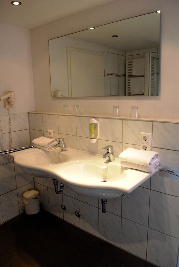 A bathroom with a large sink, two towel racks, a mirror, and a trash can.