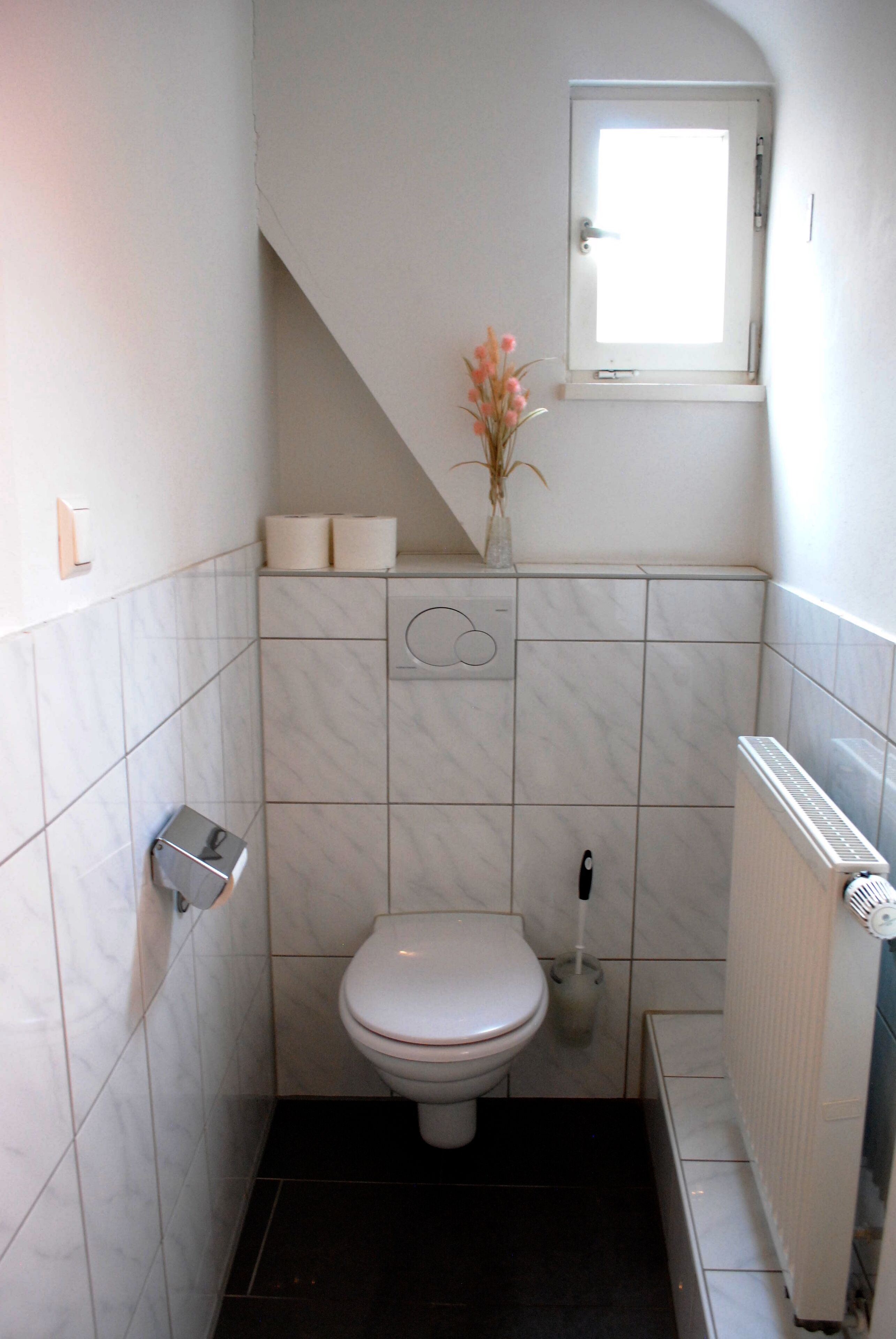 Um banheiro pequeno e moderno com vaso sanitário branco, secador de mãos e radiador.