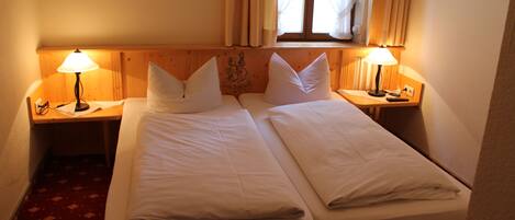 A double bed with two bedside tables, each with a lamp, in a room with a wooden headboard and a window with curtains.