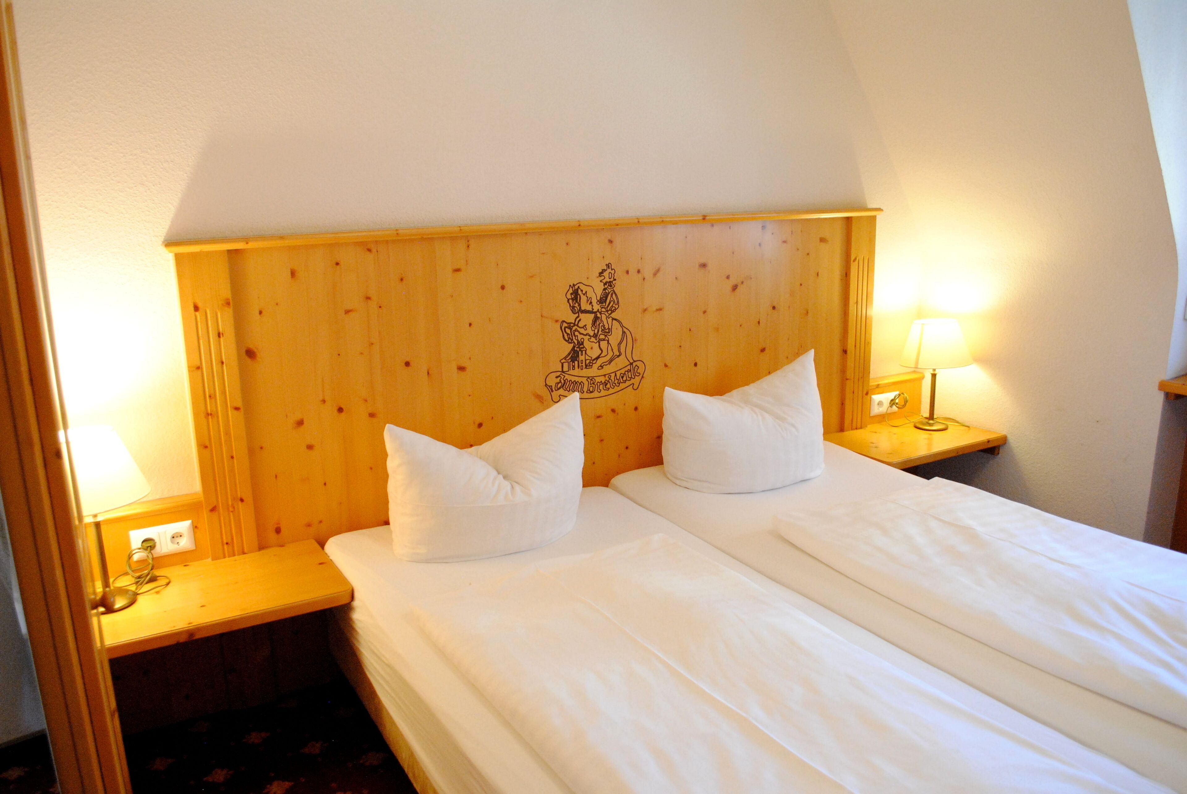 Cama doble con sábanas blancas en habitación con cabecera y mesitas de noche de madera.