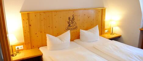 Cama doble con sábanas blancas en habitación con cabecera y mesitas de noche de madera.