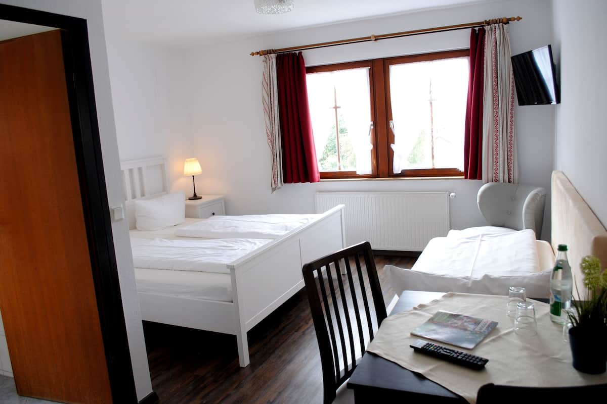 Una habitación de hotel con una cama, una silla, una mesa con un control remoto, vasos y una botella.
