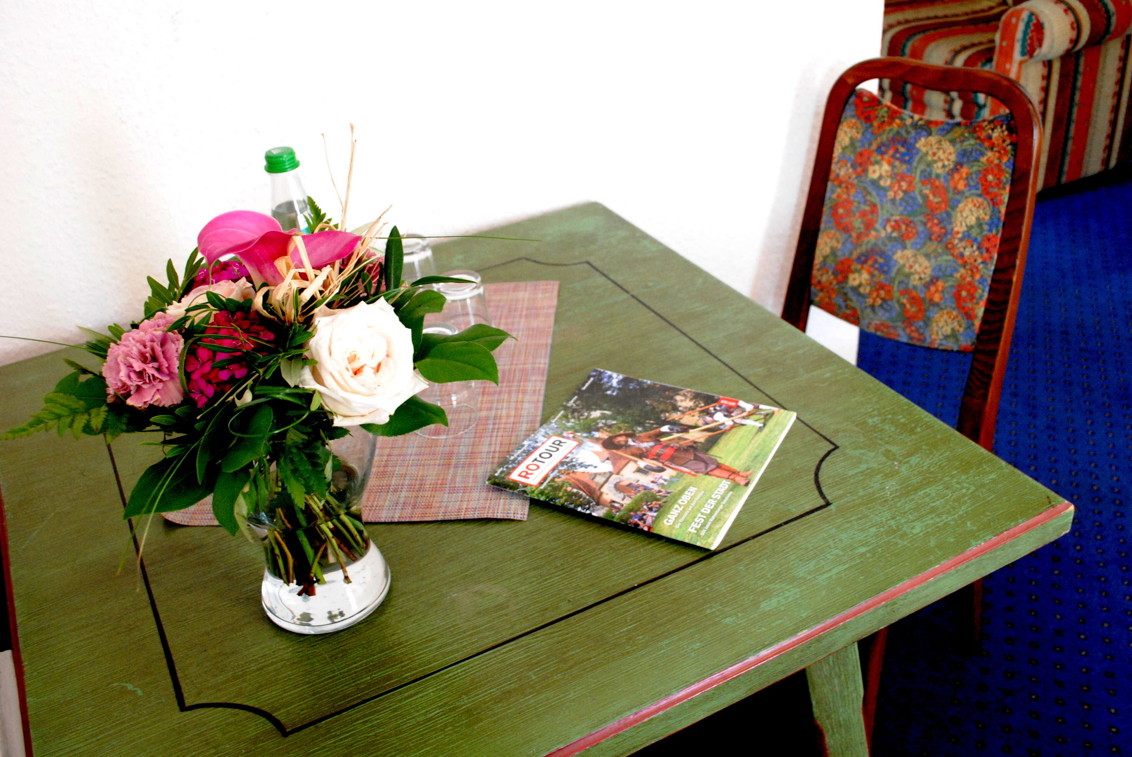 Ett grönt bord med en vas med blommor, ett glas och en tidning.