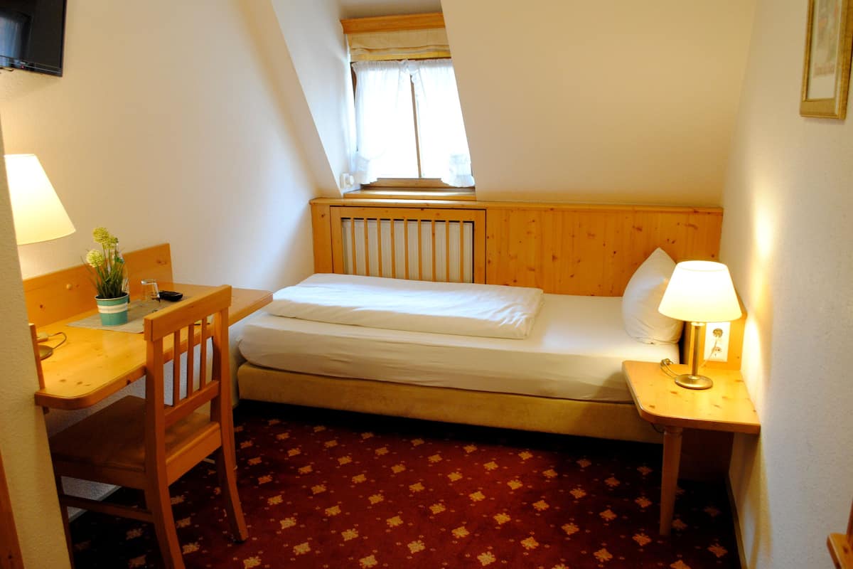 Una habitación pequeña y acogedora con cama, escritorio, silla, lámpara y ventana con cortinas.