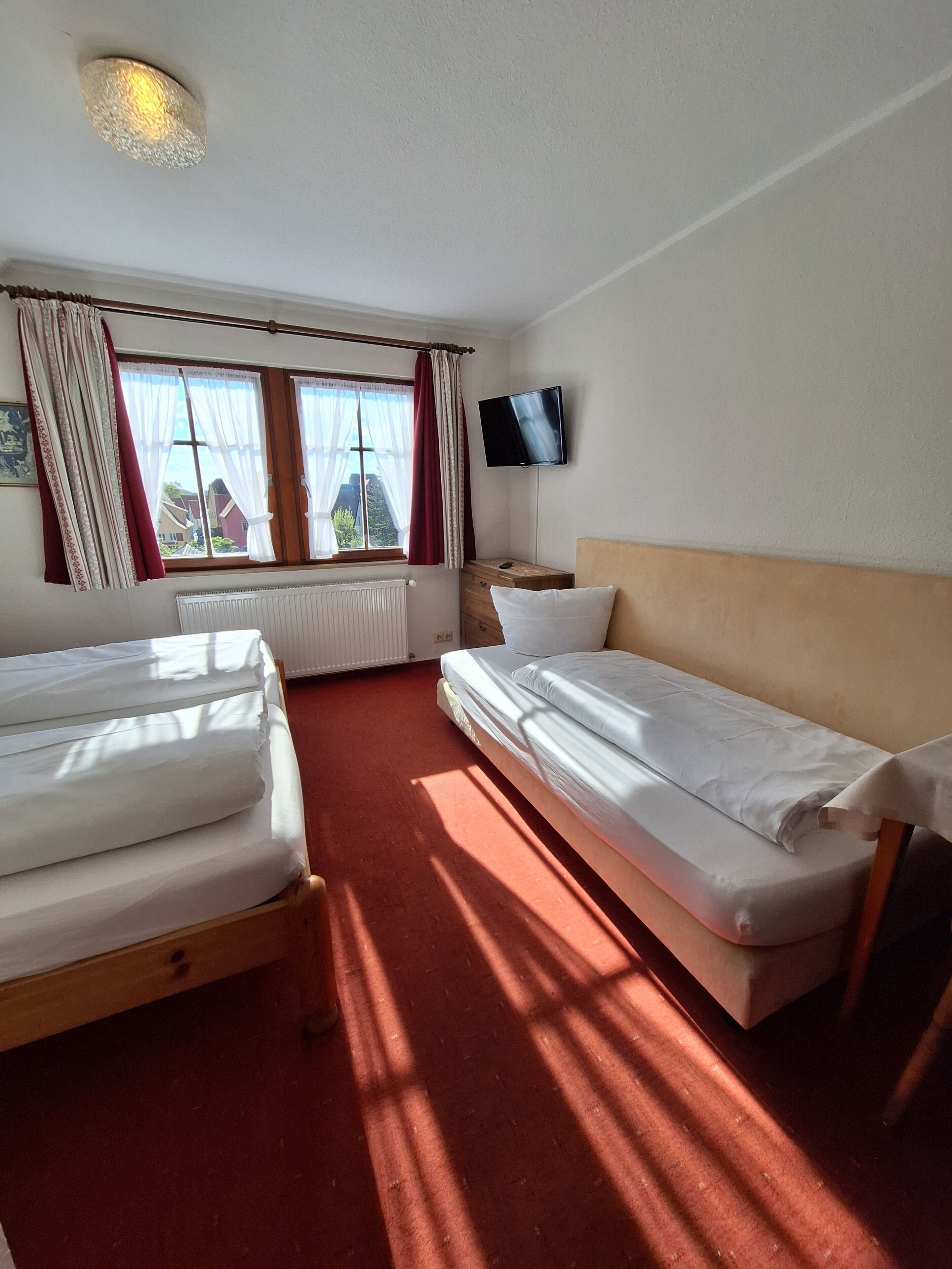 Una habitación de hotel con dos camas individuales, un televisor en la pared y una ventana con cortinas.