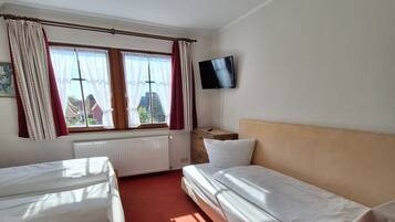 Una habitación de hotel con dos camas individuales, un televisor en la pared y una ventana con cortinas.