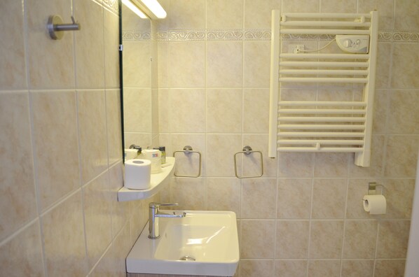 Un baño con lavamanos, espejo, toallero y papel higiénico.