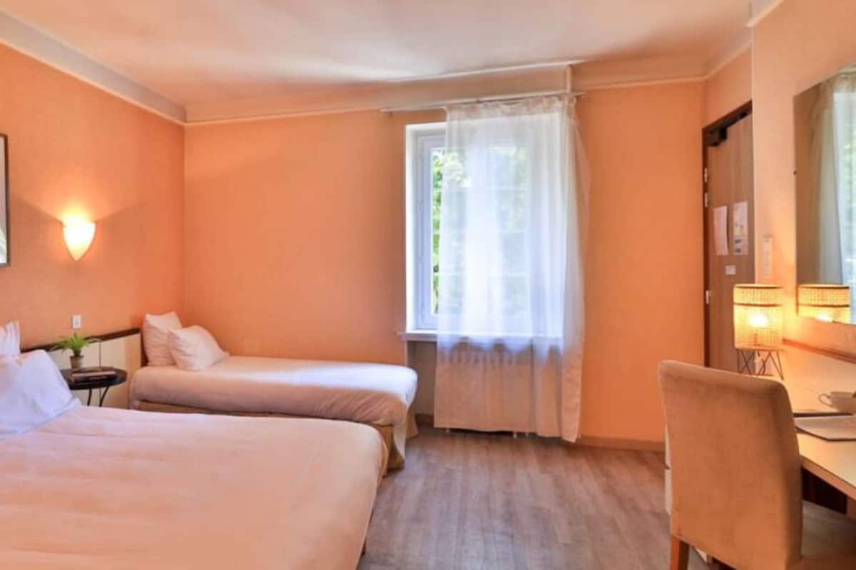 A hotel room with two beds, a desk, a chair, a lamp, and a window with curtains.