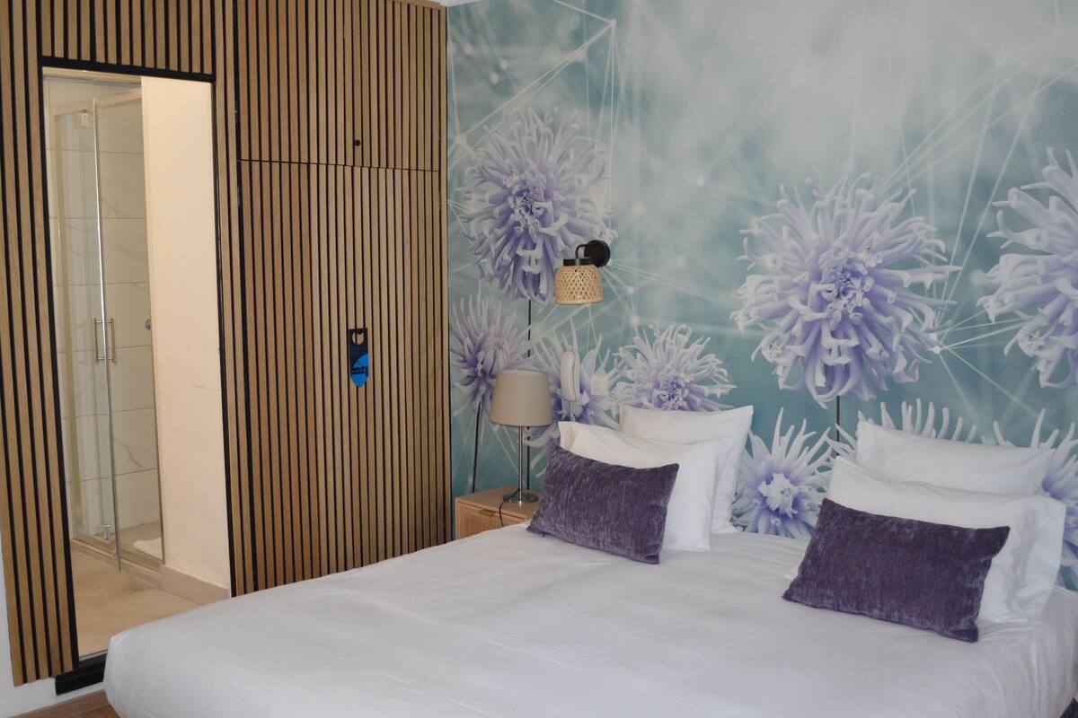 A modern hotel room with a large bed, a wooden panel wall, and a floral mural.