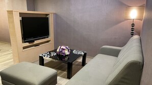 A modern living room with a flat-screen TV, a glass coffee table with a floral centerpiece, a grey sofa, and a lamp. - Beidoo Hotel (Keelung)