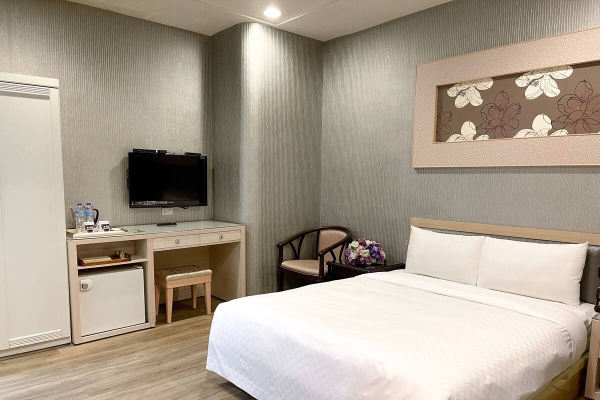 Habitación de hotel con cama, escritorio con televisor, silla y refrigerador pequeño.