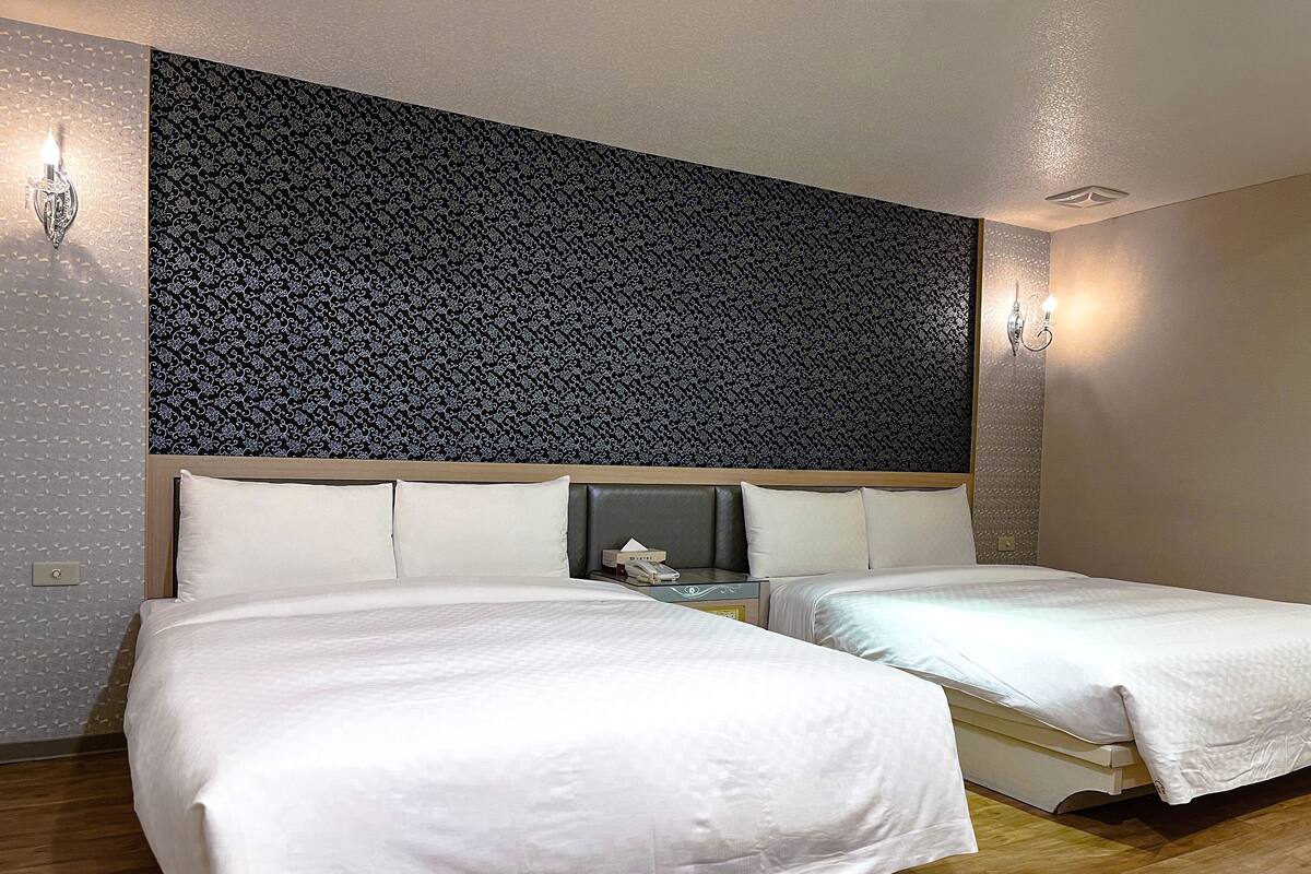 Una habitación de hotel con dos camas, un papel tapiz estampado y una mesita de noche con una lámpara.