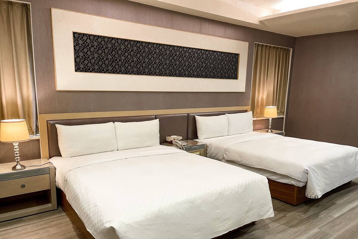 Habitación de hotel con dos camas, una obra de arte grande enmarcada sobre las camas y un cabecero de madera.