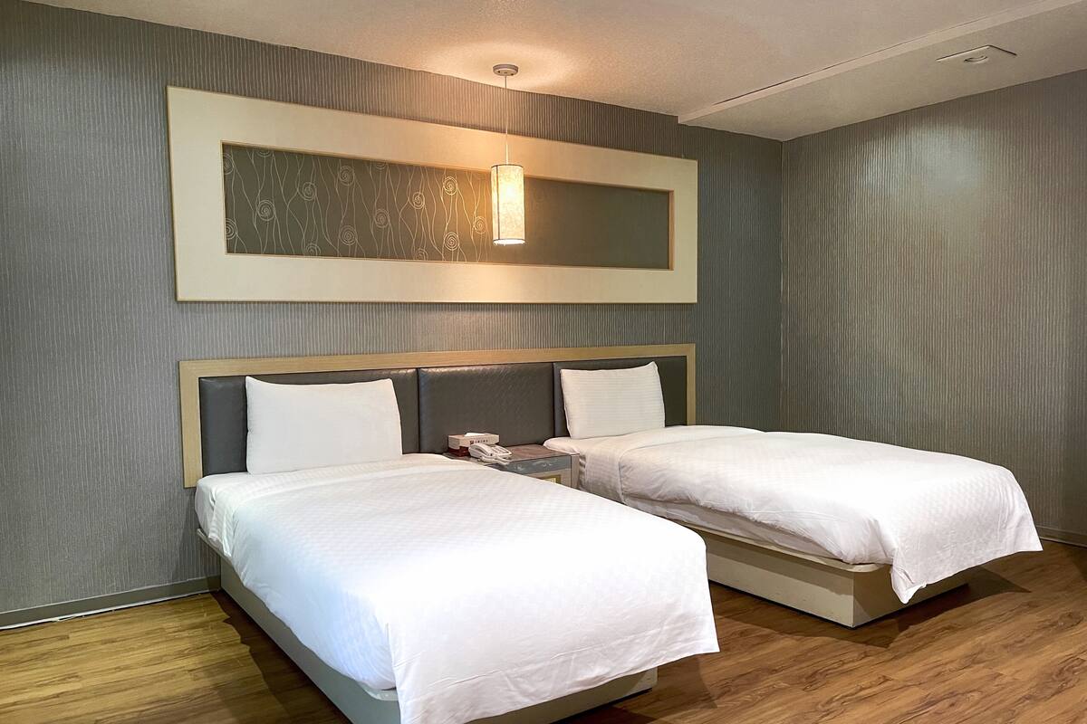 Habitación de hotel con dos camas, cabecero de madera, mesita de noche con teléfono y lámpara de pared.