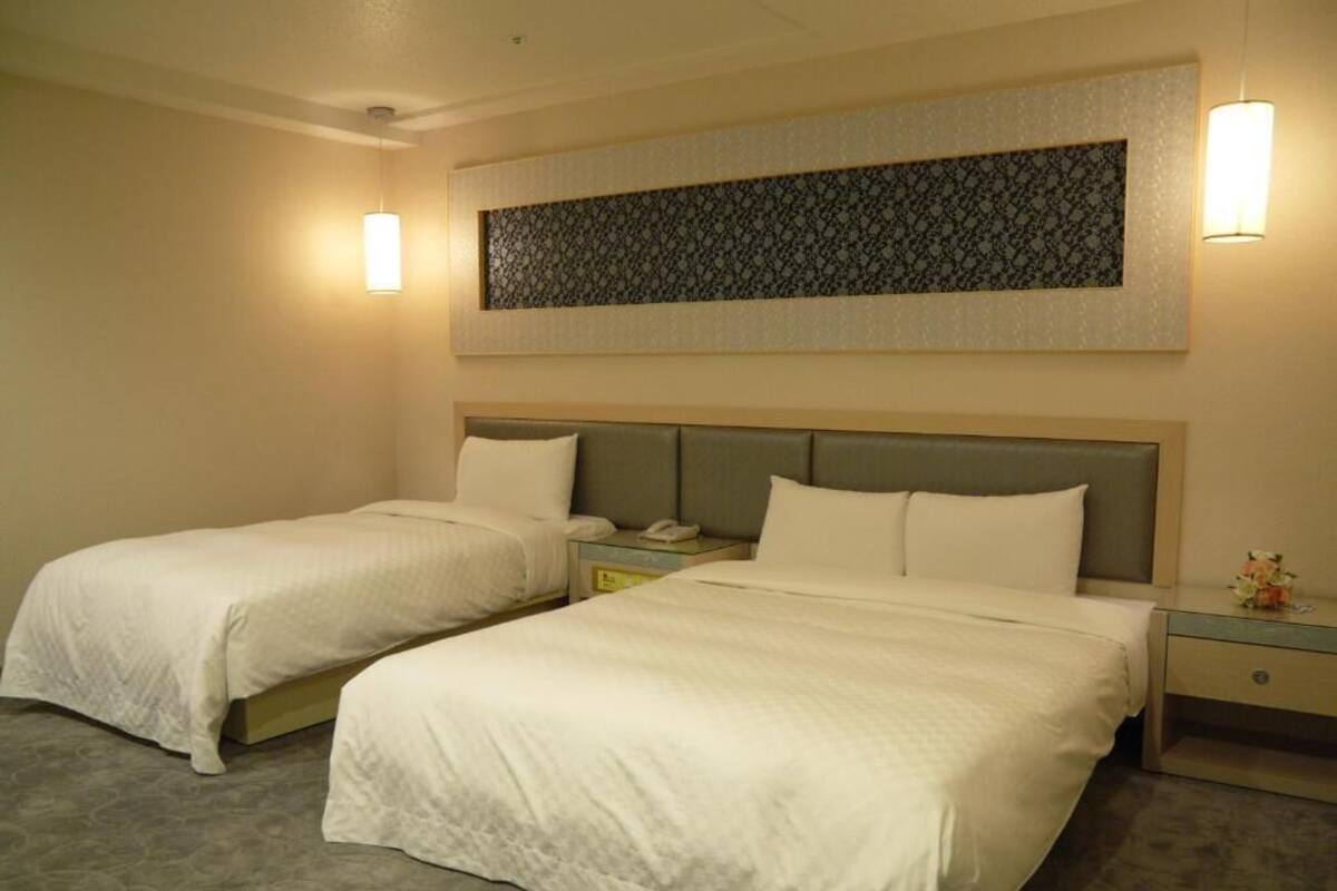 Habitación de hotel con dos camas individuales, una mesita de noche con teléfono y una obra de arte colgada en la pared.