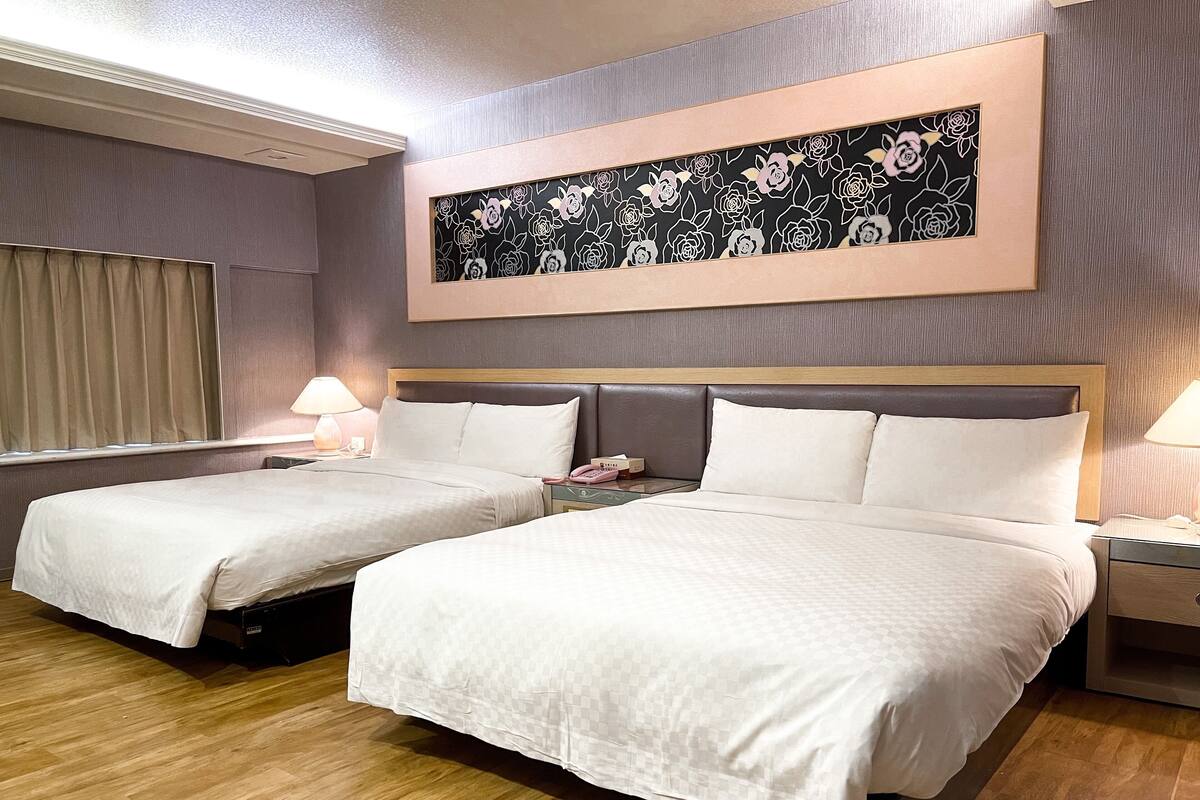 Habitación de hotel con dos camas, un cuadro floral grande encima de ellas y un cabecero de madera.