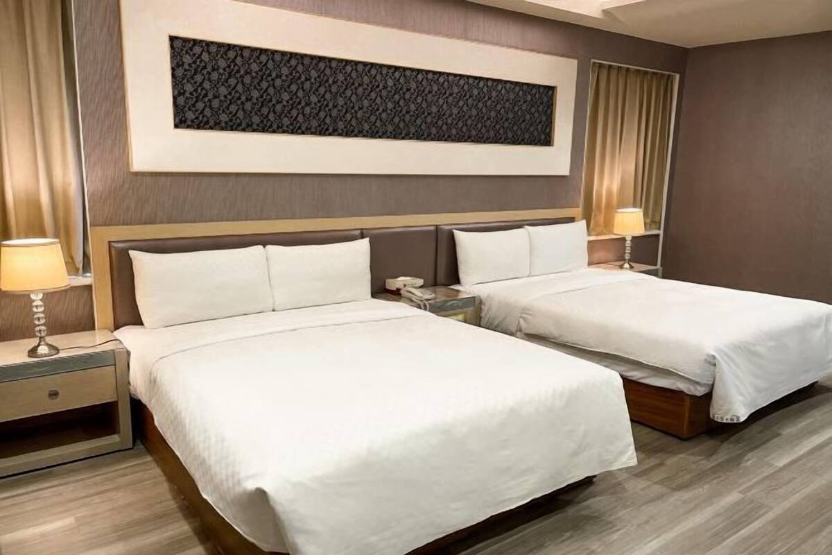 Una habitación de hotel con dos camas, una mesita de noche con lámpara, un teléfono y un panel decorativo en la pared.