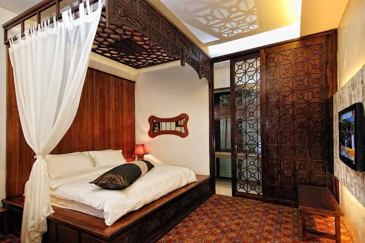 A bedroom with a four-poster bed, a wooden headboard, a patterned floor, and a TV on the wall.