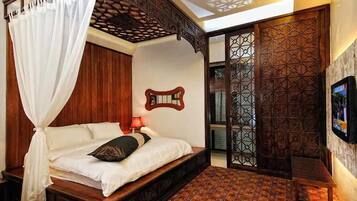 A bedroom with a four-poster bed, a wooden headboard, a patterned floor, and a TV on the wall.