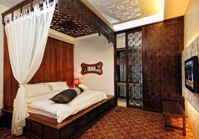 A bedroom with a four-poster bed, a wooden headboard, a patterned floor, and a TV on the wall.
