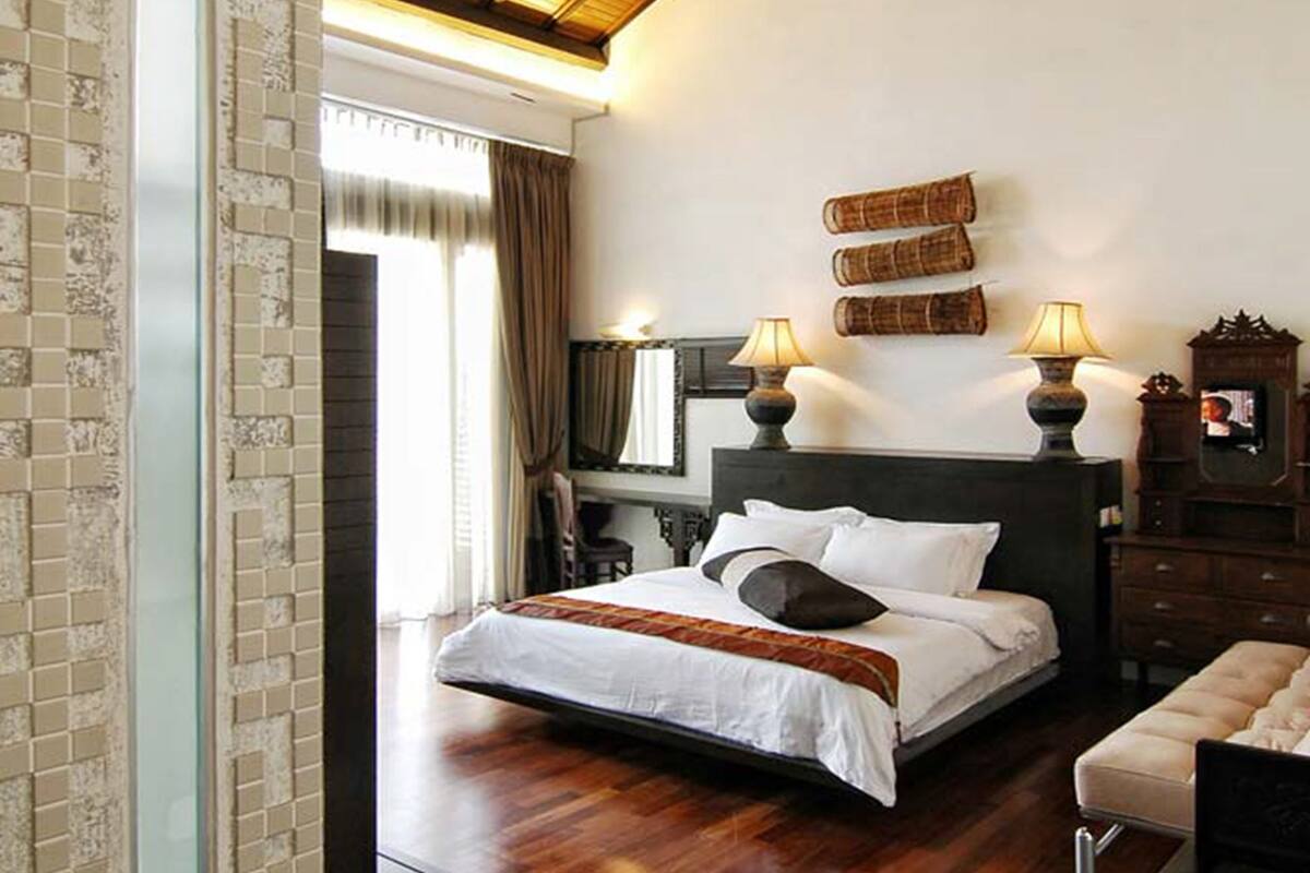 A bedroom with a wooden ceiling, a large bed with white bedding, two bedside lamps, a wooden nightstand, and a wooden dresser.