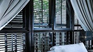 Una cama con sábanas blancas en una habitación con paredes de madera oscura y una ventana con persianas.