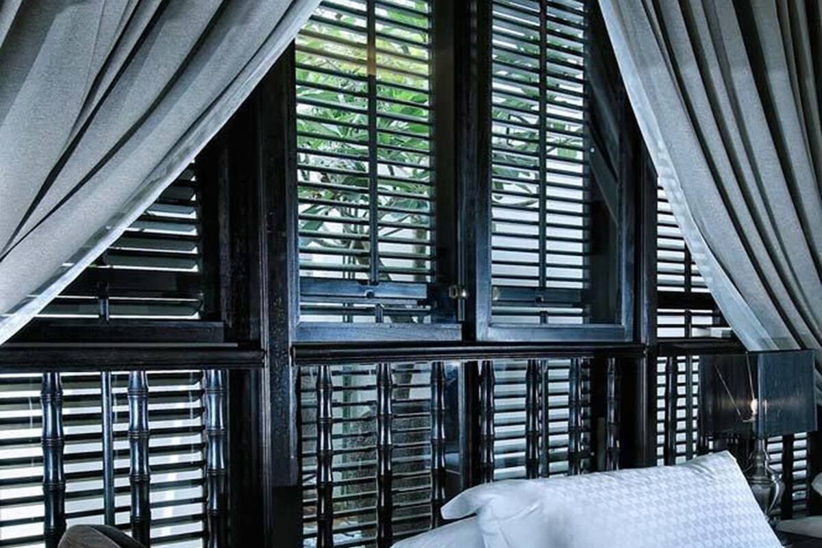 A bed with white linens in a room with black wooden walls and a window with blinds.
