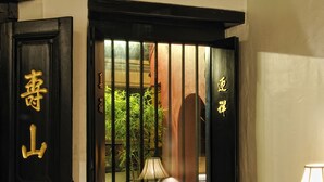 Una habitación tradicional con un banco de madera, una ventana con rejas y caracteres chinos en la pared.