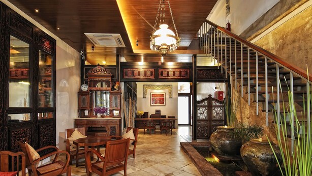 Un interior tradicional con una escalera de madera, un comedor con sillas y una mesa, y una pared decorativa con obras de arte enmarcadas.